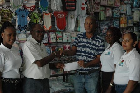 Julius Variety Store representative Leslie Mentis (2nd left) hands over the cheque to Three Peat’s Rawle Welch in the presence of staffers on Tuesday at their Regent Street location
