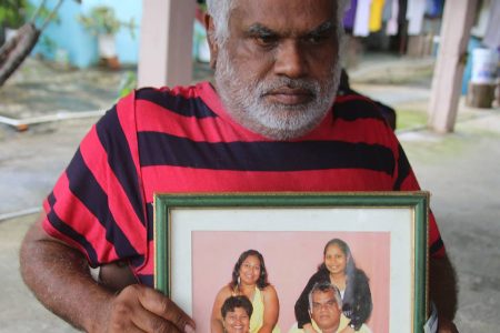 Rajendra Basdeo holds a family photo with his wife Lutchmin Rampersad-Basdeo and daughters Aarti and Annurada at his home in Rousillac yesterday. Lutchmin and Aarti died in a car crash on Friday.