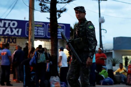 An army soldier patrols on a street next to people from Venezuela after checking their passports or identity cards at the Pacaraima border control, Roraima state, Brazil Aug. 19, 2018. Nacho Doce—Reuters