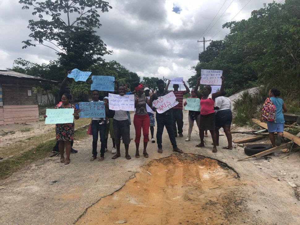 Parents and residents of Kuru Kuru, Soesdyke-Linden Highway, with their placards yesterday, standing in front of the first pothole at the start of the access road.
