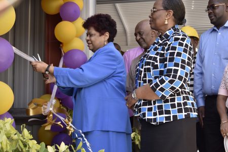 Minister of Social Protection,  Amna Ally cutting the ceremonial ribbon to commission the new elevator, as Junior Minister, Keith Scott and Permanent Secretary, Lorene Baird  and other officials look on. (Ministry of the Presidency photo) 
