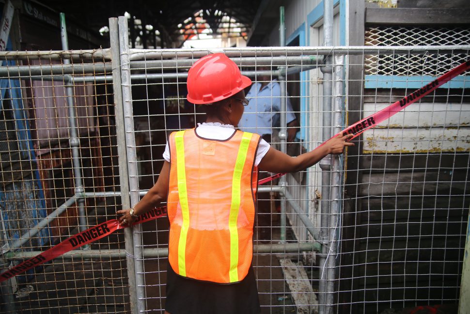 A city occupational health and safety officer placing tape on one of the barricades restricting access to the Stabroek Market Wharf. (Photo by Terrence Thompson)