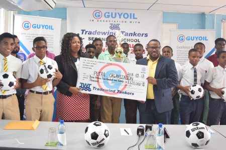Petra Organization Co-Director Troy Mendonca (third from right) collecting the sponsorship cheque from GuyOil Marketing and Sales Manager Jacqueline James following the launch of the Secondary Schools U18 Football League. Also in the photo are students of some of the participating teams

