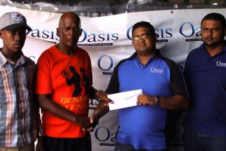 The Guyana Beverage Company’s Brand Manager, Raymond Govinda (2nd right) hands over the sponsorship cheque to race organizer and head coach of the FACC Randolph Roberts. 