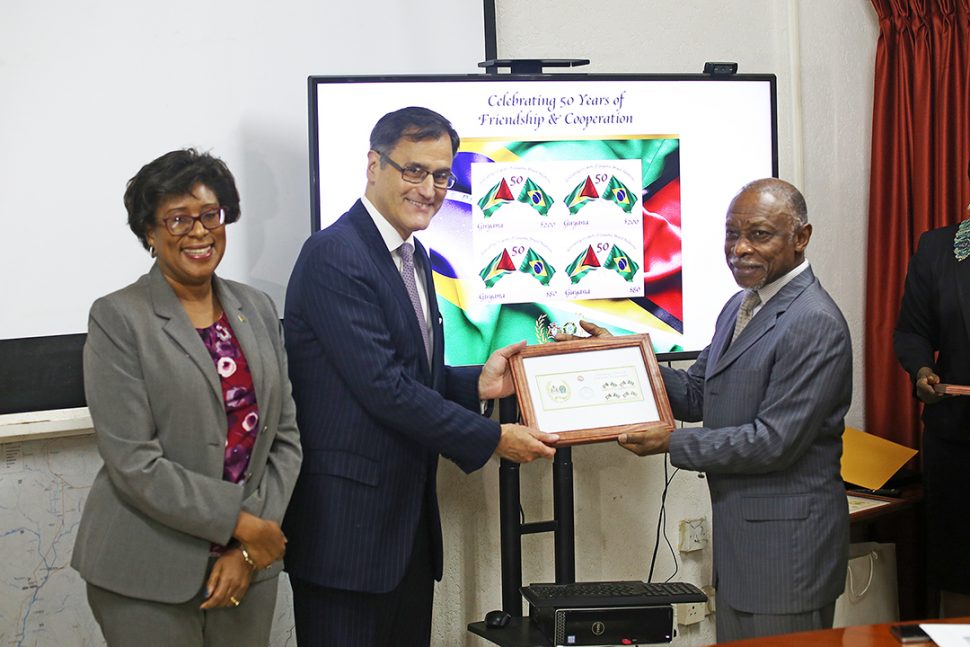 Minister of Foreign Affairs Carl Greenidge (right) presents Deputy Head of Mission of the Embassy of Brazil Paulo Silos with First Day Covers of the commemorative stamp issued to mark the 50th Anniversary of bilateral relations between Guyana and Brazil. Minister of Public Telecommunications Cathy Hughes looks on at left. (Photo by Terrence Thompson) 