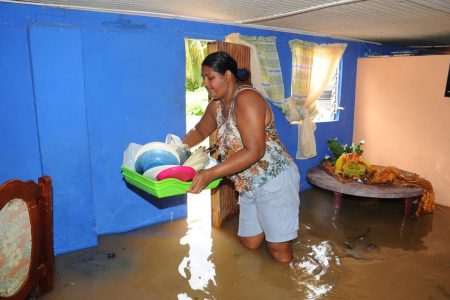 A woman remove kitchen items from her flooded home in Kelly Village, Caroni, on Sunday. 