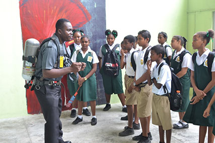Fire safety: As part of activities for fire prevention week, the Guyana Fire Service (GFS) on Friday hosted a fire safety fair for students along the East Bank Demerara (EBD) at the Providence Stadium, according to the Department of Public Information (DPI).
Fire Prevention Officer of the GFS, Nigel Gravesande, told DPI, “We want a safety conscious environment and we need to start first with our children because they are the ones who will have to change the environment in terms of safety. We will sensitize them on fire, fire behaviour and what to do in those situations”.
This DPI photo shows one of the fire officers explaining his work. 