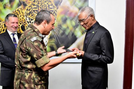 Colonel Nilton de Figueiredo Lampert, Commanding Officer of the Brazilian Jungle Warfare Training Centre (CIGS), presenting the Jungle Warrior Machete No. 353 to President David Granger at State House yesterday as Brazil’s Ambassador to Guyana, Lineu Pupo de Paula, looks on. The Ministry of the Presidency said President Granger received the machete by virtue of the training he received at CIGS in 1969. (Ministry of the Presidency photo)