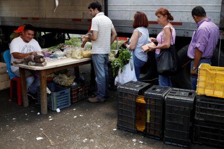 A vendor uses a point-of-sale (POS) device as people wait in line at a vegetable and fruit stall at a street market in Caracas, Venezuela October 8, 2018. REUTERS/Marco Bello