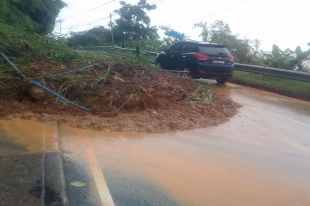 A vehicle makes its way around a landslide along the Western Main Road in Carenage this evening.