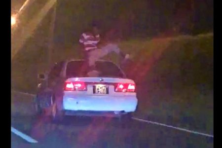 A screenshot of the video showing the man riding on top of a car on the highway.