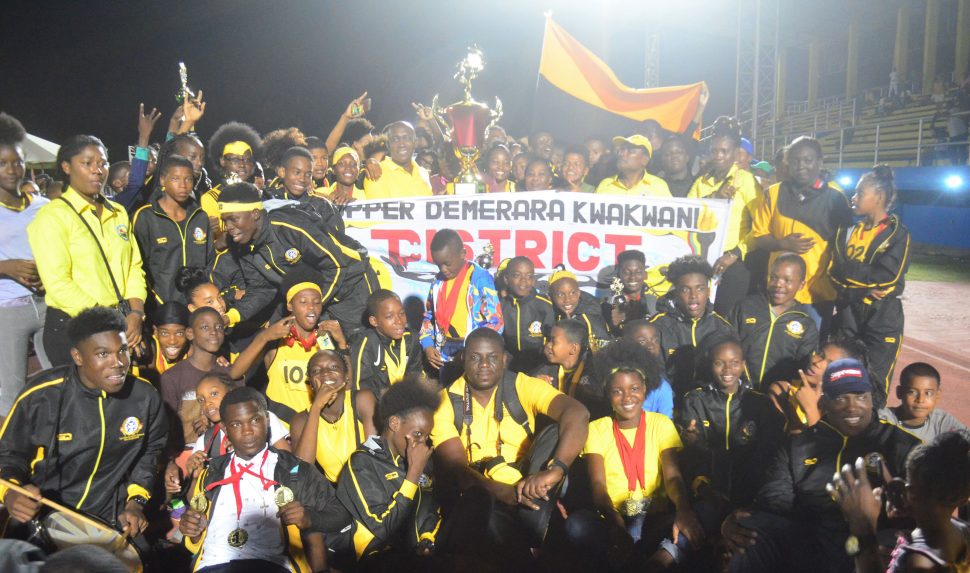 Athletes and officials of Upper Demerara/Kwakwani celebrating last evening at the National Track and Field Centre with the Champions of Champions trophy with Non-Alcoholic Brand Manager from Banks DIH Limited, Clayton McKenzie. (Orlando Charles photo) 