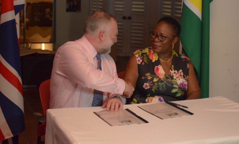 National Hydrographer of the UK Hydrographic Office, Rear Admiral Tim Lowe, and the Director General of the Maritime Administration Department, Claudette Rogers shake hands shortly after signing the data release statement.  (Department of Public Information photo)   