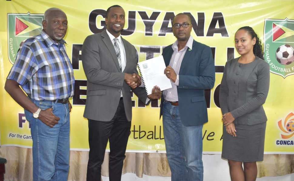 GFF President Wayne Forde (2nd right) presenting the Disciplinary Code to GFF Disciplinary Committee Chairman Roger Yearwood in the presence of two other committee members.