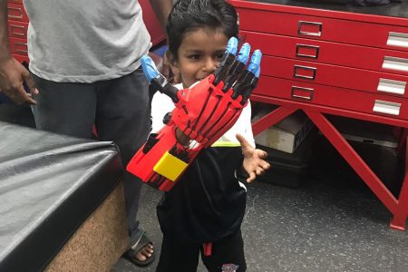 Joshua Rufus plays with an “Iron Man” prosthetic hand at Qualitech Machining Services Ltd in Point Lisas where local engineers will build him a 3D printed prosthetic arm in the coming weeks.