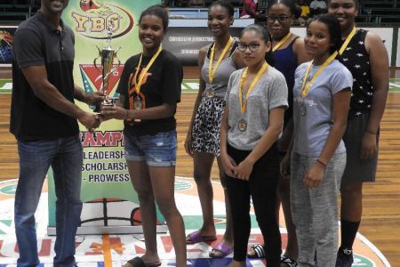 Marian Academy captain Jada Mohan, receives the championship trophy in the presence of team-mates, after Marian Academy defeated Kwakwani in the girls final of the Titan Bowl Basketball Championships at the Cliff Anderson Sports Hall Sunday.
