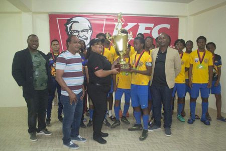 Shiva Boys Hindu School of Trinidad and Tobago captain receives the championship trophy from the KFC representative in the presence of teammates, after they defeated Christianburg/Wismar to complete a perfect campaign in the inaugural KFC Goodwill Football Championship at the Ministry of Education ground Saturday night. 