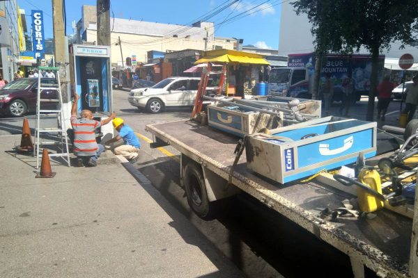 TELEPHONE LOVE: These two men dismantle one of the telephone booths on Frederick Street, Port of Spain. 