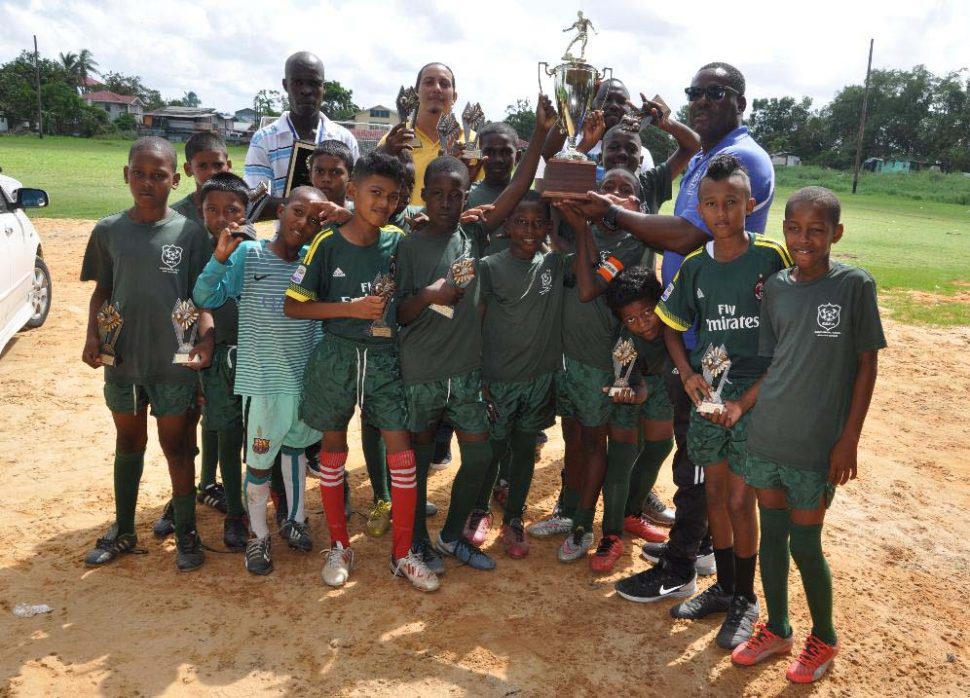 Omar Sam, captain of newly crowned champion Timehri Panthers, collecting the championship trophy from EBFA President Franklin Wilson in the presence of his team-mates after defeating Friendship on the final matchday of the Ralph Green u11 League
