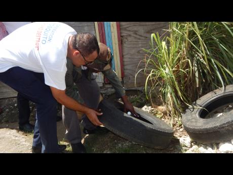Minister of Health Dr Christopher Tufton examines an old tyre with a health worker during an islandwide vector clean-up operation.