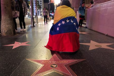 A woman with a Venezuelan flag wrapped around her shoulders kneels behind a paper star reading "Juan Guaido President of Venezuela" placed on the Walk of Fame during a demonstration in Hollywood on Jan. 23, 2019.