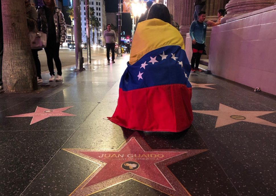 A woman with a Venezuelan flag wrapped around her shoulders kneels behind a paper star reading “Juan Guaido President of Venezuela” placed on the Walk of Fame during a demonstration in Hollywood on Jan. 23, 2019.