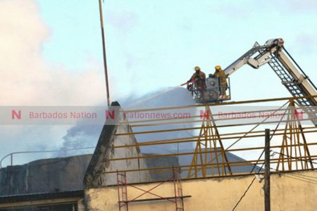 Firemen using the combination platform ladder to spray foam in the burning tank at Mount Gay Rum Distillery yesterday. (Picture by Ricardo Leacock.)