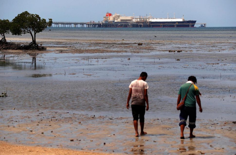 Locals walk along a small beach where a Liquefied Natural Gas (LNG) carrier called Kumul is docked at the marine facility of the ExxonMobil PNG Limited operated LNG plant at Caution Bay, located on the outskirts of Port Moresby in Papua New Guinea, November 19, 2018. Picture taken November 19, 2018. REUTERS/David Gray
