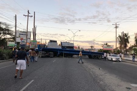 This Department of Public Information photo shows the container truck blocking three of the four lanes on the EBD highway at McDoom and commuters walking past heading to Georgetown. 