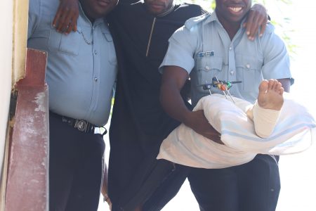 Rodrick Thomas, one of the two men accused of fatally shooting taxi driver Kelvin Walters before he ran them over with his car, being assisted out of a city courtroom by two policemen yesterday. Thomas was charged with the crime yesterday, while his co-accused remains hospitialised. (Photo by Terrence Thompson)