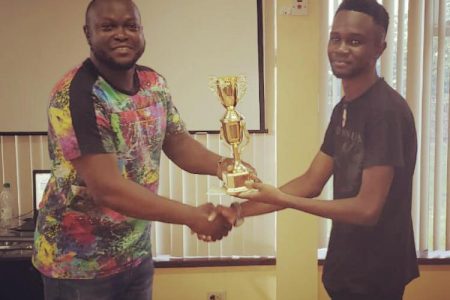 President of the Guyana Chess Federation James Bond (left) presents the winner of last Saturday’s chess tournament Davion Mars with his trophy at the National Resource Centre. Mars, a student of the University of Guyana, overcame a field of enthusiastic players to be crowned champion of the one-day tournament.