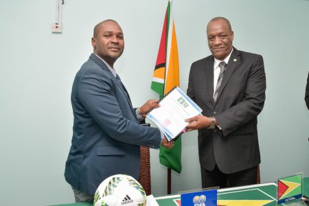 Minister of State,  Joseph Harmon (right) hands over a copy of the Memorandum of Understanding to President of the Guyana Football Federation, Wayne Forde. (Ministry of the Presidency photo)