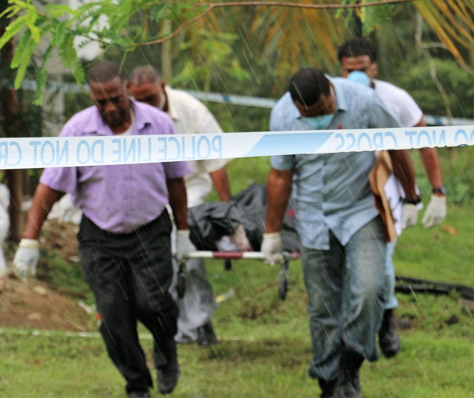 Undertakers and police officers remove the body of Nigel Charles from his garden at Coalmine, Sangre Grande, on Friday.