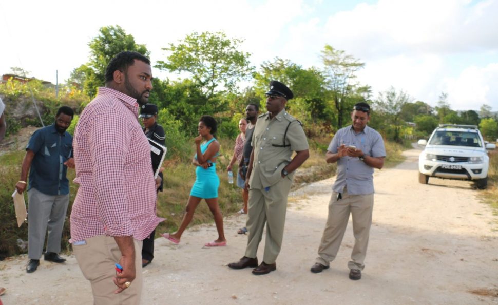 Police officers and villagers mingle on the road outside the property of Trevor Johnson, who was chopped to death by another villager yesterday.