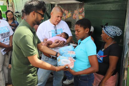 Mayor Ubraj Narine presenting a resident of Tiger Bay with diapers, while Social Cohesion Minister George Norton assists by holding the woman’s sleeping child. (Terrence Thompson photo)