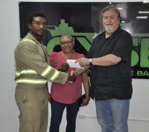 General Manager of Guyana Shore Base Inc Mark Edwards (right) presents the sponsorship cheque to Carlos Petterson-Griffith (left) in the presence of physiotherapist Kathleen Paul.
