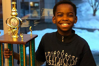 Eight-year-old Tanitoluwa Adewumi, an immigrant from Nigeria who currently resides in New York, poses with his trophy. He captured the New York State Primary Chess Championship in the kindergarten-to-third-grade bracket. ‘Tani’, as he is familiarly called, played undefeated in the Championship, where he outmaneuvered his opponents from elegant private schools with pricey chess tutors. Tani learnt chess a little over a year ago. (Photo: GoFundMe) 
