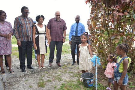Young resident of Timehri North, Princess Rutherford symbolically turns on a tap in her community while GWI, BNTF and Regional officials look on (GWI photo)