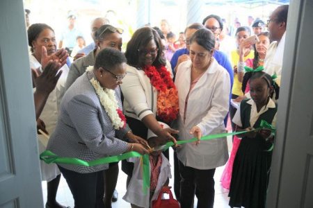 Ministers of Public Health Hon. Volda Lawrence and Dr. Karen Cummings help a child to cut the ribbon to officially open the Plegt Anker Health Centre. (DPI photo)