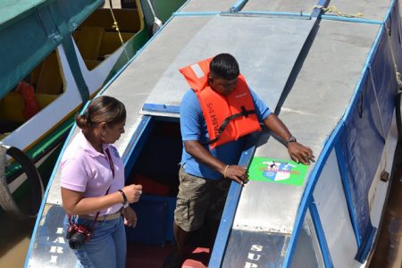 A boat operator placing the MARAD sticker on his boat at the Parika Stelling. (DPI photo)