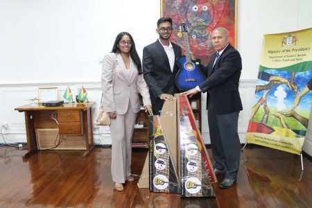 Minister George Norton (right) accepts five brand new guitars from Chandini and Khishan Singh, representatives of Gaico Construction and General Services Incorporated. (Ministry of Social Cohesion photo)