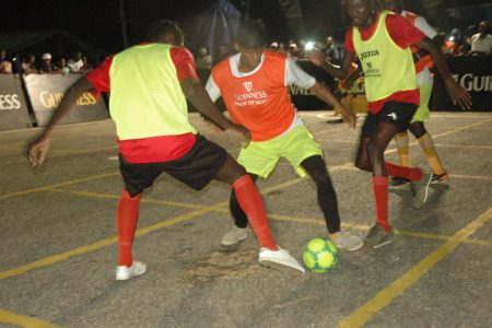 Melanie-B goal scorer Odell Gulliver [center] trying to maintain possession while being sandwiched between two Liliendaal Hustlers players at the Haslington market Tarmac in the Guinness ‘Greatest of the Streets’ East Coast Demerara Championship Saturday.