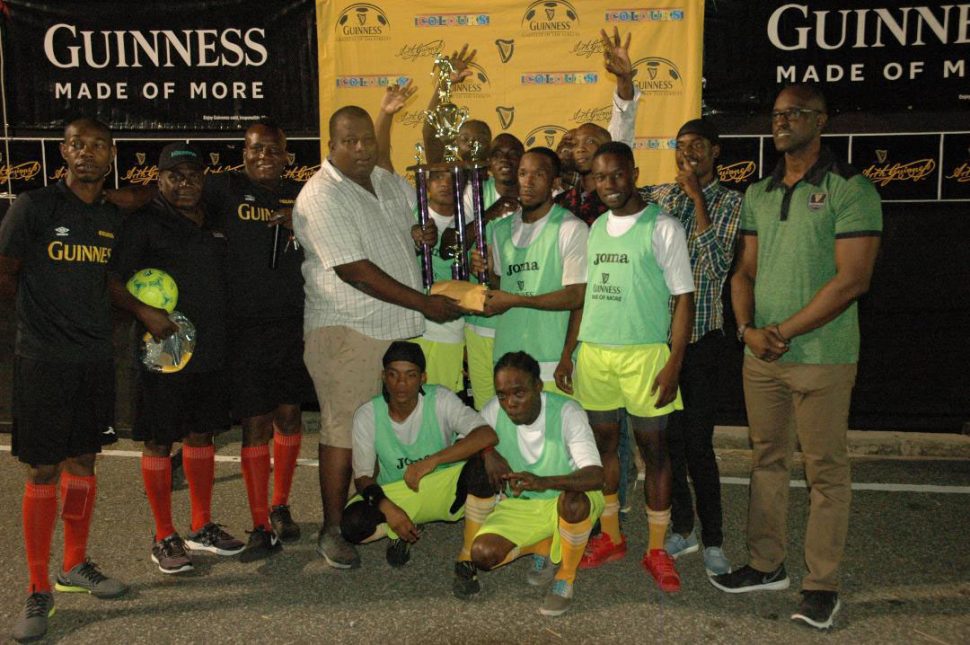 Melanie `B’ Captain Ryan Seales receives the championship trophy from Banks DIH Limited representative Evlon Hendy in the presence of his team-mates following their victory over Paradise `A’ in the final of the Guinness ‘Greatest of the Streets’ East Coast Demerara Championship. Also in the photo is Guinness Brand Manager Lee Baptiste [right] 
