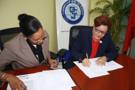 Registrar and Chief Marshal of the Caribbean Court of Justice,  Jacqueline Graham (left) watches as Justice Maureen Rajnauth-Lee affixes her signature to the revised Rules of Court in the Original and the Appellate Jurisdiction. (CCJ photo)
