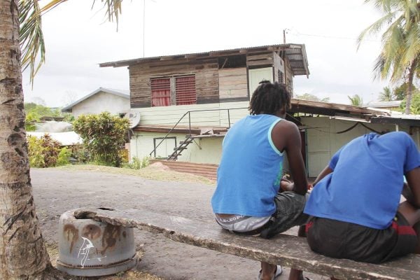 Two men sit on a makeshift bench opposite the house where Leslie Forrester, 57, his common-law wife Jennifer Alexander, 55, and daughter Lizann Forrester, 30, were chopped by a man known to them in Palo Seco. All three are warded in serious condition at the SFGH. Photo by Lincoln Holder