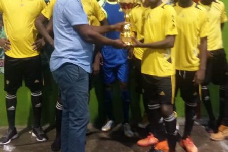 Pernell Schultz of Bent Street collects the championship trophy from tournament coordinator Frank ‘English’ Parris after they defeated Gold is Money 6-5 in the finale of the Stag Beer Futsal Championship at the National Gymnasium, Mandela Avenue

