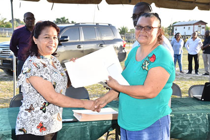 Minister of State Dawn Hastings-Williams (left) handing over one of the agreements. (Ministry of the Presidency photo)