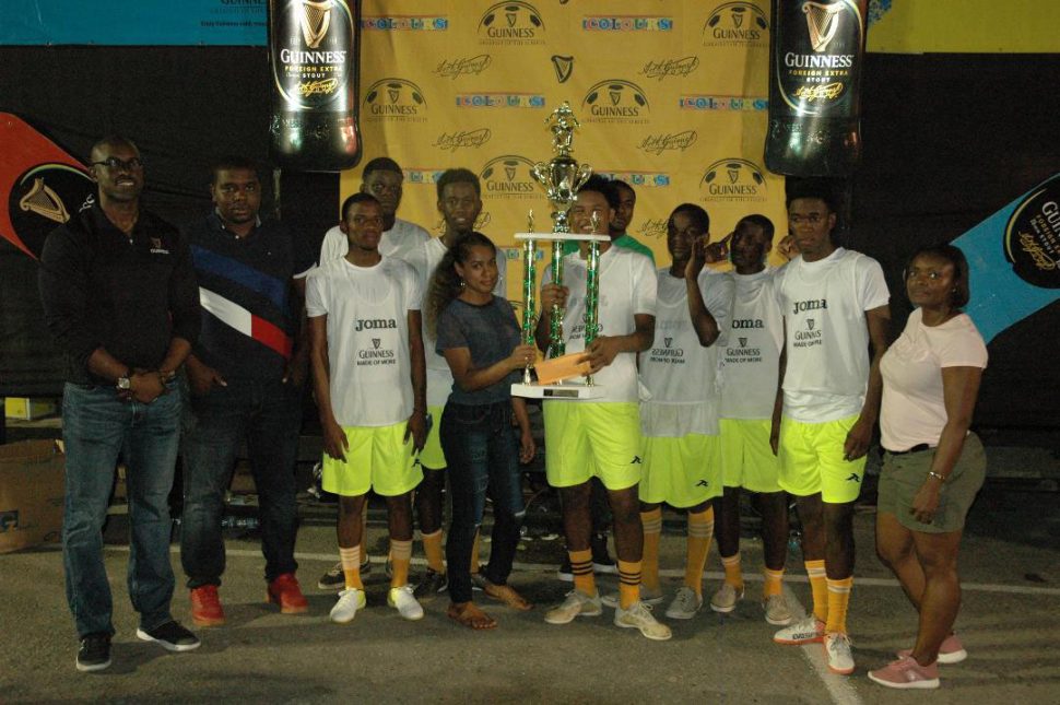 High Rollers captain Omar Brewley [center], receives the championship trophy from Banks DIH representative Romaine Adonis in the presence of his elated team-mates after they defeated  Amazings in the final of the Guinness Greatest of the Streets Linden Championship. Also in the photo are Guinness Brand Manager Lee Baptiste [left] and Linden Branch Manager Shondel Easton [right]
