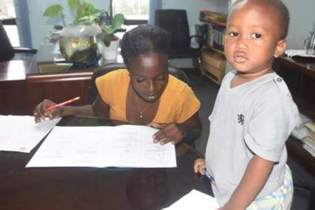 Ackaisha Green completing an assessment paper at the HEART Trust/NTA head office on Oxford Road in Kingston yesterday, while her son Joshua looks on. (Photo: Naphtali Junior)