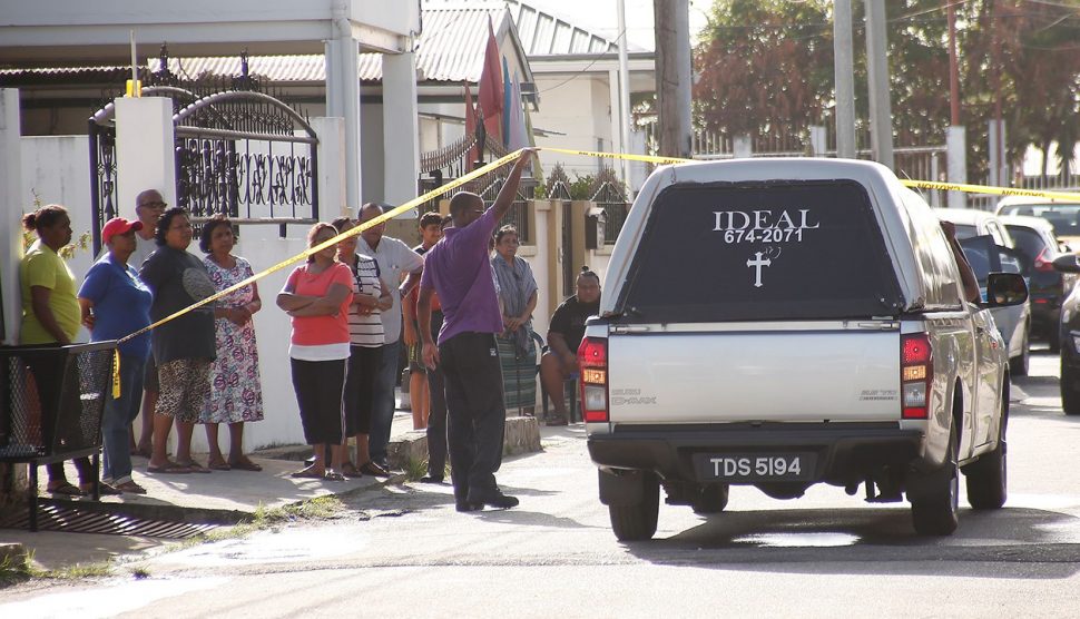 A crowd looks on as members of the Singh family who died in a fire at their Samaroo Street, Aranguez, home yesterday, are taken away by undertakers.